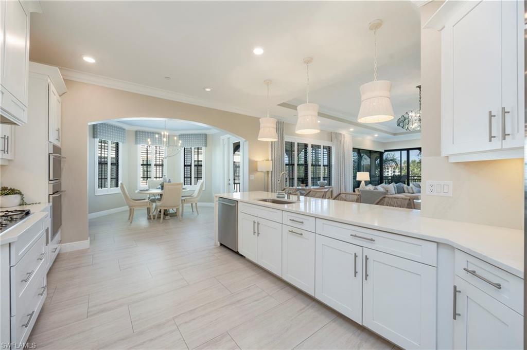 16351 Viansa Way, Unit 202 Naples, FL 34110 - Photo 7 of 35 Kitchen with white cabinets, a peninsula, crown molding, hanging lights, and light stone countertops