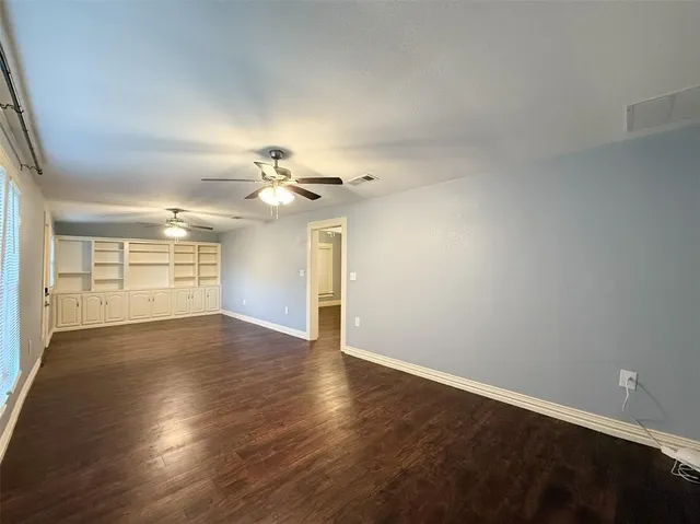 an empty room with wooden floor chandelier fan and windows