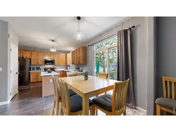 a kitchen with stainless steel appliances kitchen island granite countertop a refrigerator a stove a sink a dining table and chairs with wooden floor