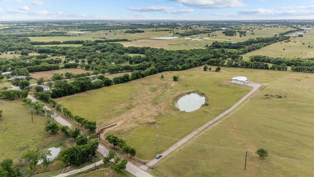 1161 Alsdorf Road Ennis, TX 75119 - Photo 5 of 28 Expansive rural landscape featuring a private pond, open fields, a long gravel driveway, and a large metal outbuilding