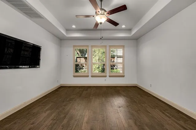 an empty room with wooden floor ceiling fan and windows