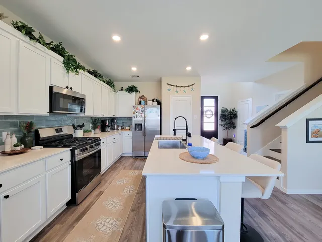 a large white dining hall with stainless steel appliances granite countertop a stove oven a refrigerator with white cabinets and wooden floor