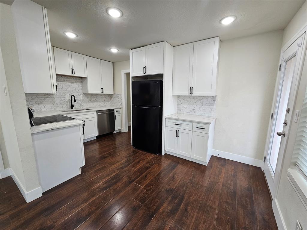 211 North Hampton Road Dallas, TX 75208 - Photo 8 of 22 Contemporary kitchen featuring abundant white cabinetry, contrasting dark wood-finish flooring, a black refrigerator, stainless steel dishwasher, and a black faucet over a sink