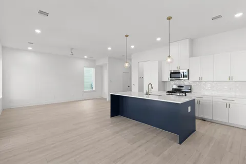 a large kitchen with stainless steel appliances granite countertop a stove a sink a refrigerator and white cabinets with wooden floor