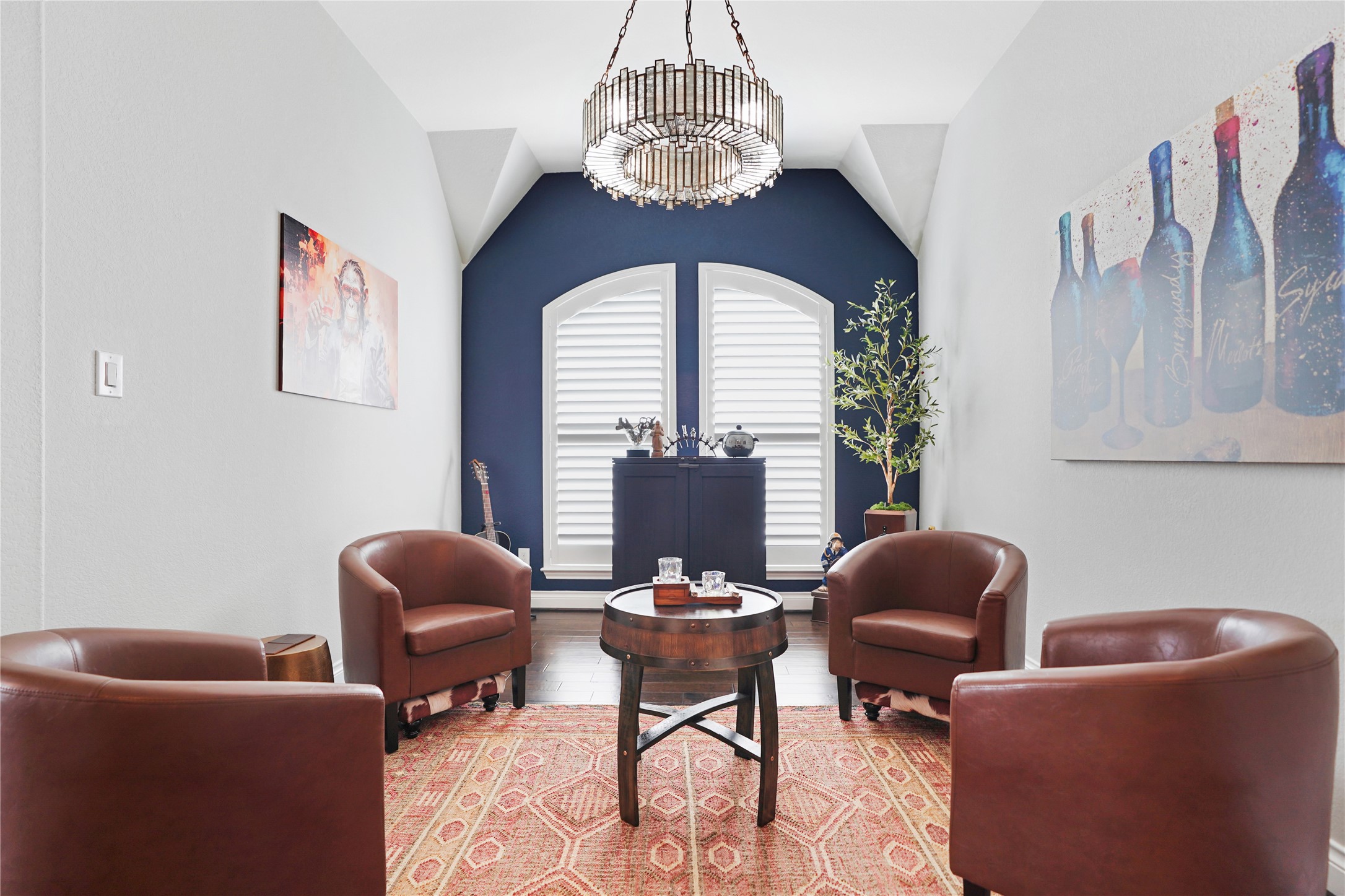 2345 Redwood Ridge Trail Manvel, TX 77578 - Photo 8 of 39 This cozy sitting area features four brown leather chairs around a small round table, with a modern chandelier overhead. The room is accented by a bold blue wall with arched windows, artwork, and a plant, creating a stylish and inviting space.