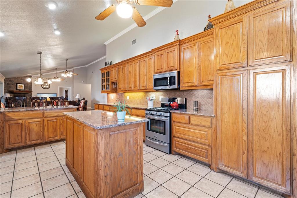 20175 Willow Glade Circle Pilot Point, TX 76258 - Photo 9 of 32 Kitchen featuring tasteful backsplash, light tile patterned flooring, crown molding, a kitchen island, and appliances with stainless steel finishes