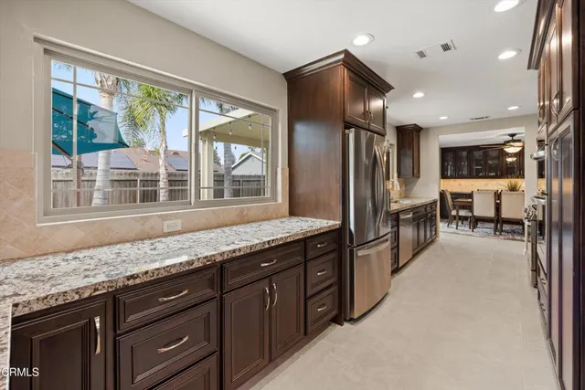 a kitchen with stainless steel appliances granite countertop a refrigerator a stove and a sink with large window