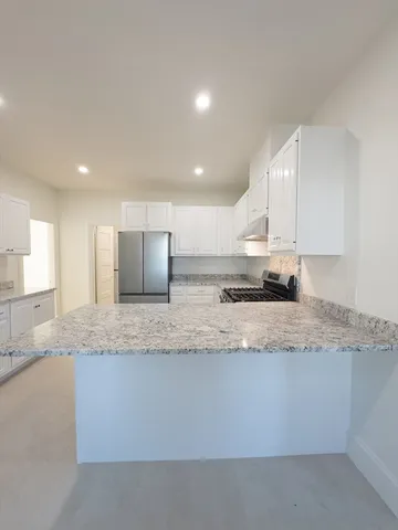 a large kitchen with granite countertop a large counter top stainless steel appliances and cabinets