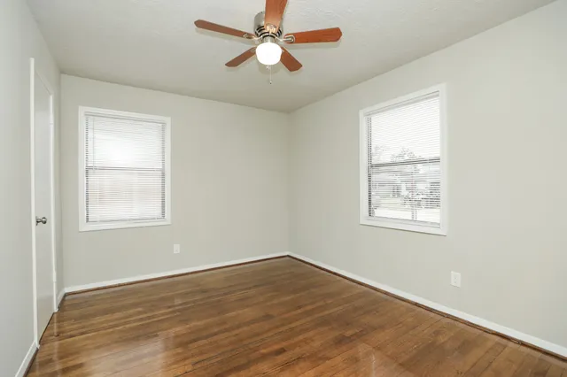 an empty room with wooden floor chandelier fan and windows