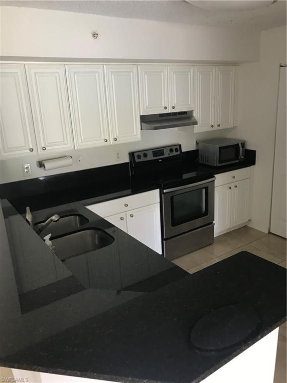 8245 Ibis Club Drive, Unit 409 Naples, FL 34104 - Photo 14 of 18 a kitchen with granite countertop white cabinets and black appliances