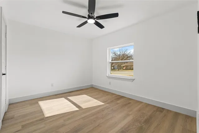 an empty room with wooden floor ceiling fan and windows