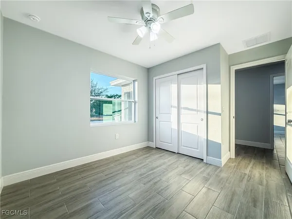 an empty room with wooden floor chandelier fan and windows