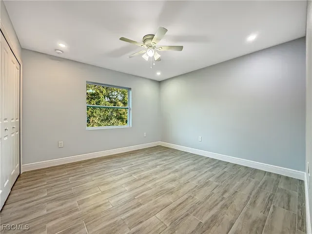an empty room with wooden floor chandelier fan and windows