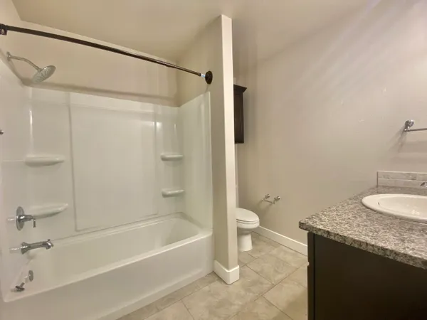a bathroom with a granite countertop bathtub shower sink vanity and toilet