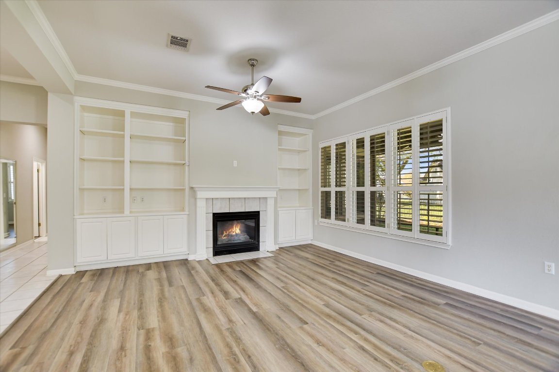 126 Bass Street Georgetown, TX 78633 - Photo 5 of 20 Unfurnished living room featuring crown molding, built in shelves, light wood finished floors, a fireplace, and a ceiling fan