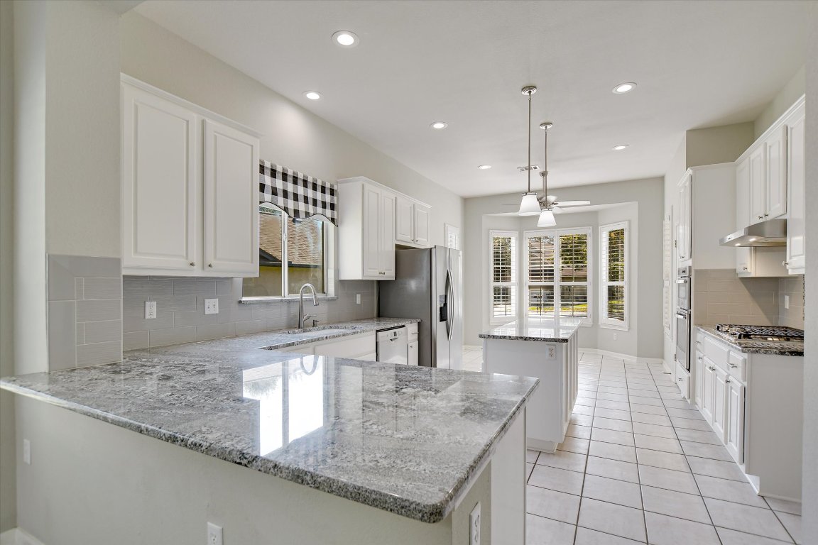 126 Bass Street Georgetown, TX 78633 - Photo 10 of 20 Kitchen featuring backsplash, white cabinetry, light stone counters, light tile patterned floors, and recessed lighting
