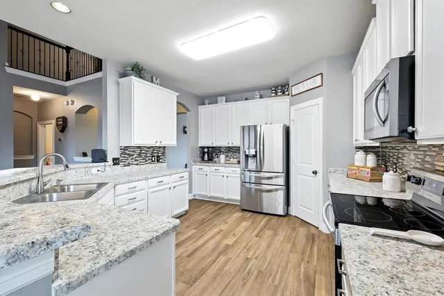 a large kitchen with a refrigerator a stove a sink dishwasher a oven with white cabinets and wooden floor