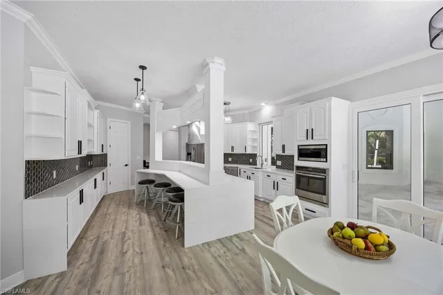 a kitchen with stainless steel appliances a stove a sink a refrigerator and a dining table with wooden floor