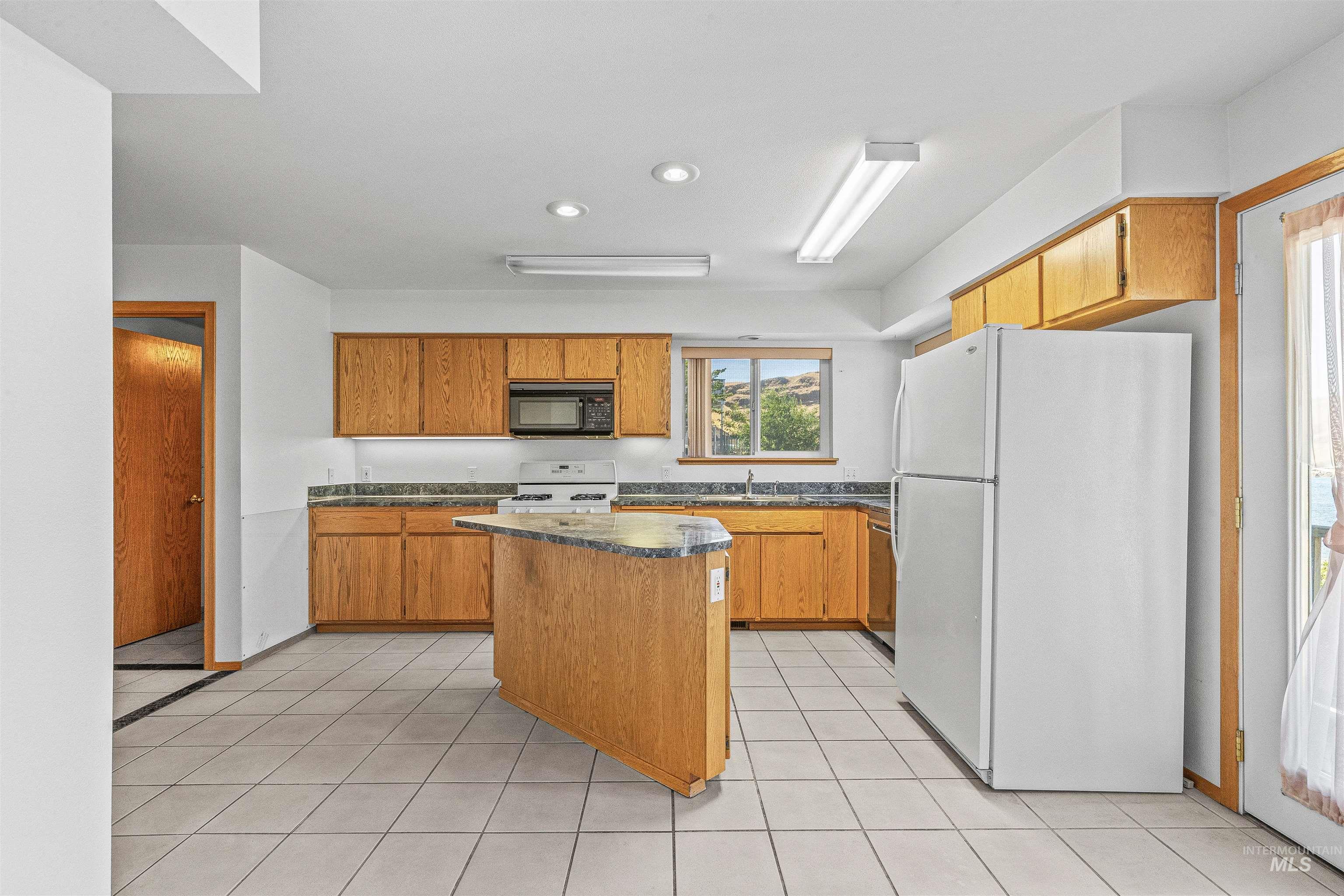 1962 Golfview Drive Clarkston, WA 99403 - Photo 17 of 35 Kitchen with white appliances, a kitchen island, dark countertops, recessed lighting, and light tile patterned floors