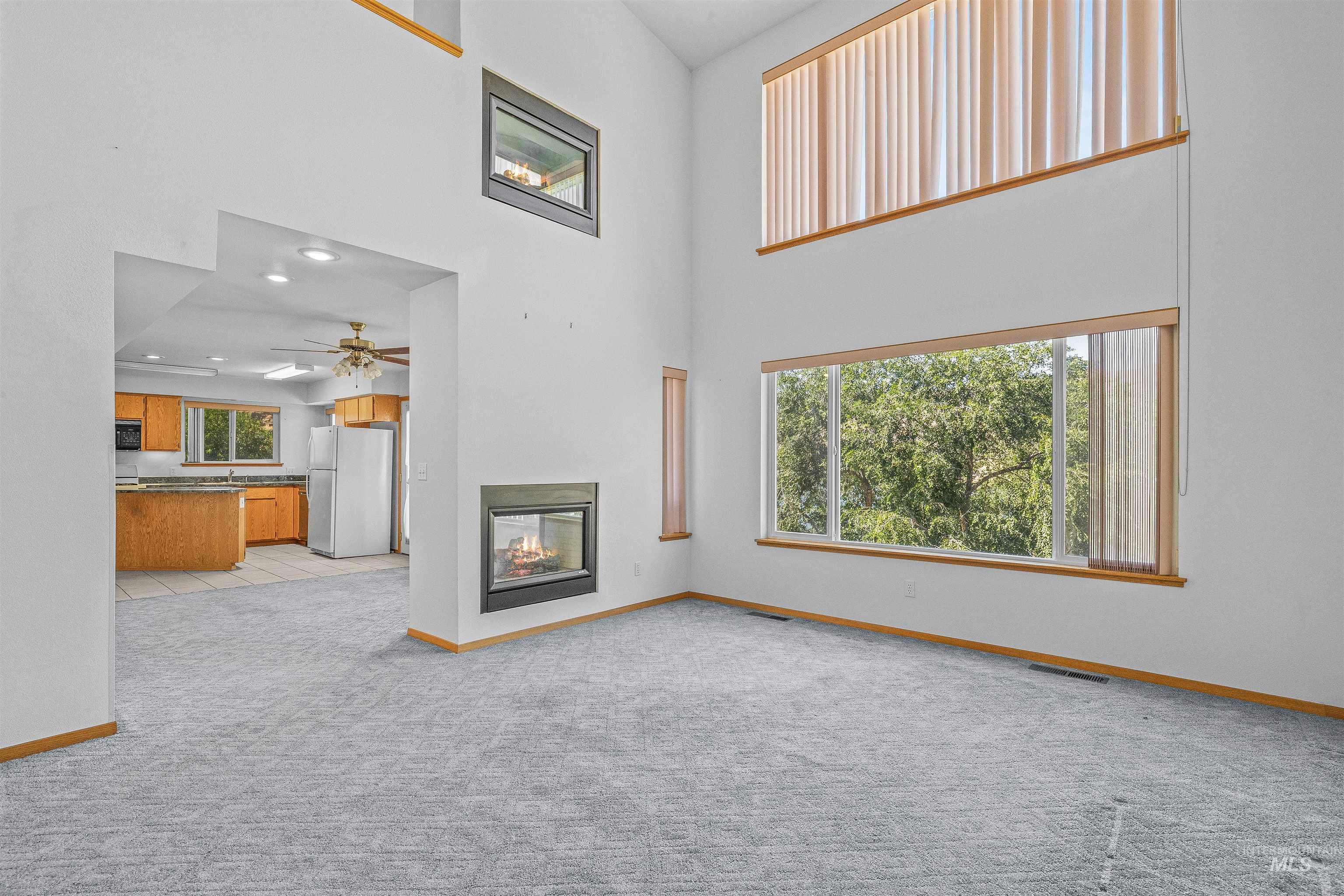 1962 Golfview Drive Clarkston, WA 99403 - Photo 21 of 35 Unfurnished living room with plenty of natural light, light carpet, a towering ceiling, a ceiling fan, and a multi sided fireplace