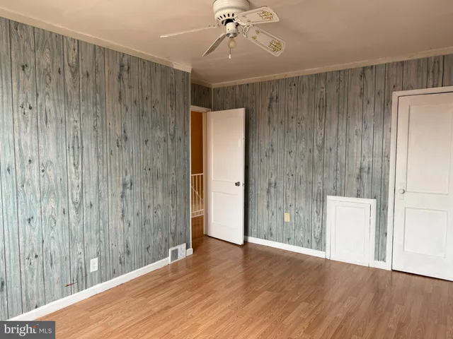 a view of an empty room with wooden floor and a ceiling fan