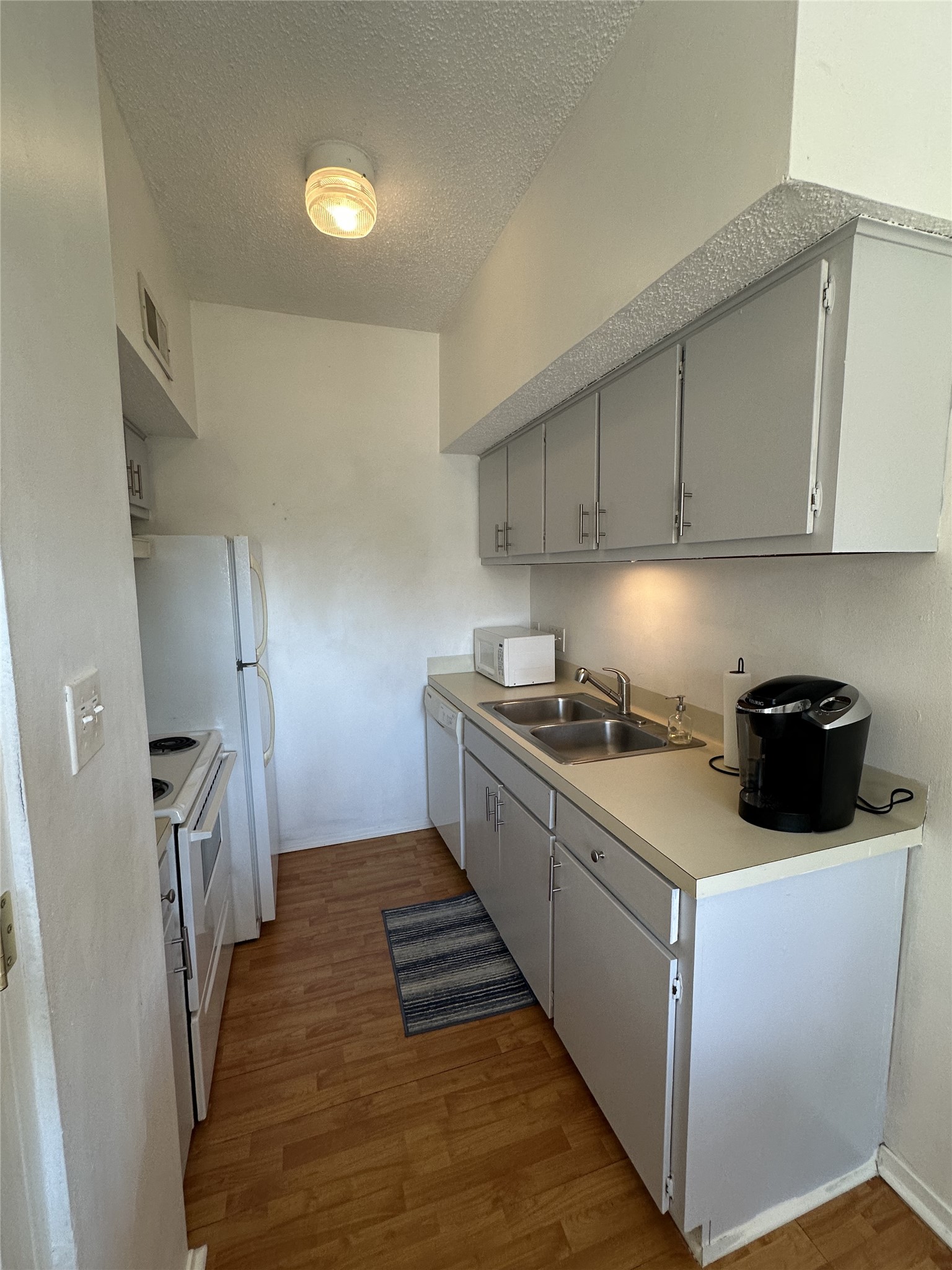 3316 Guadalupe Street, Unit 306 Austin, TX 78705 - Photo 25 of 28 Kitchen featuring gray cabinetry, a textured ceiling, light wood-style flooring, white appliances, and light countertops
