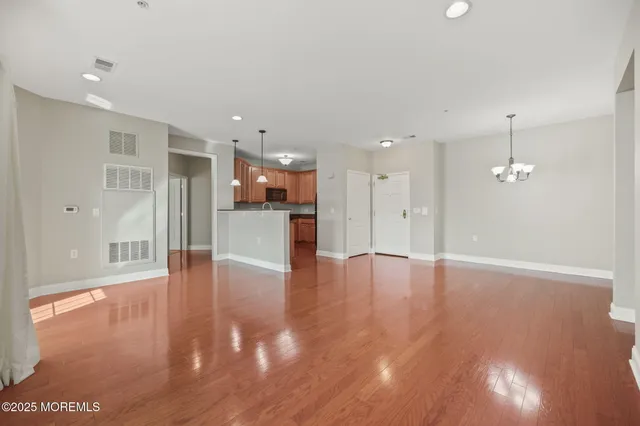 a view of an empty room with wooden floor and a kitchen