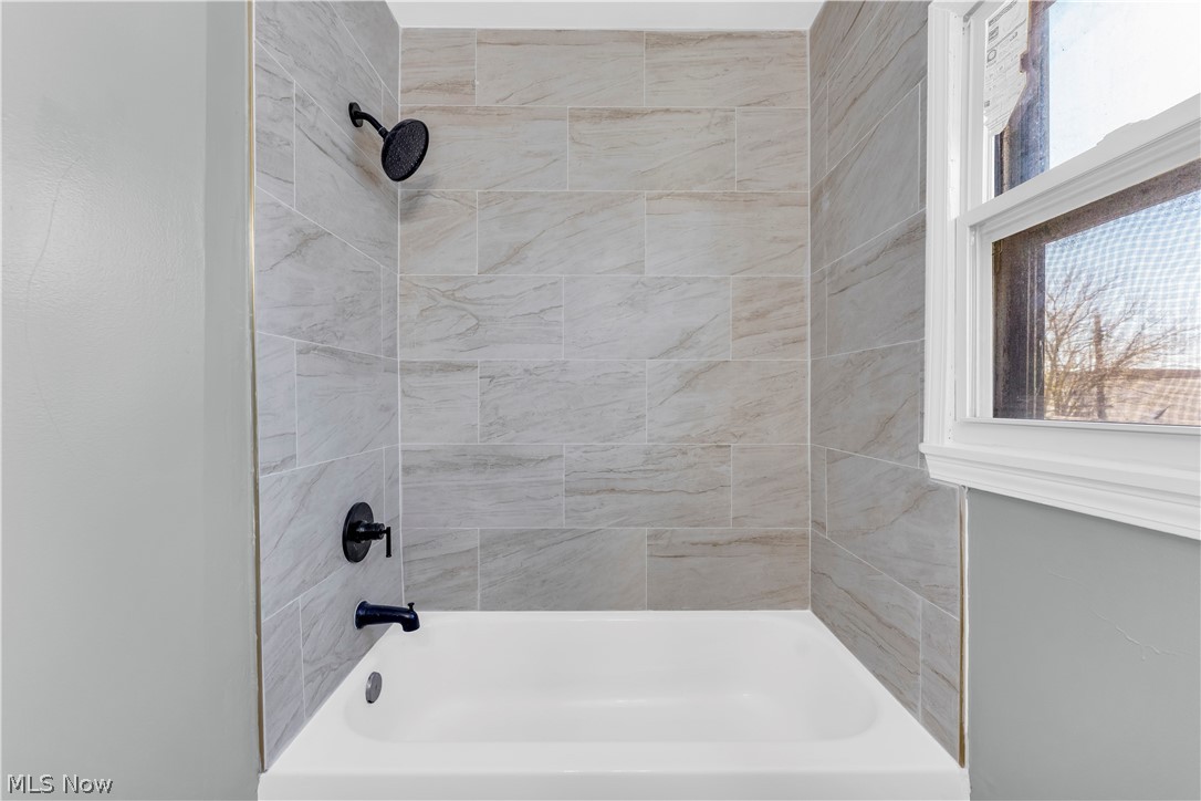 12808 Havana Road Cleveland, OH 44125 - Photo 16 of 19 Bathtub and shower combination featuring a white tub, matte black shower fixtures, and light-toned tile surround