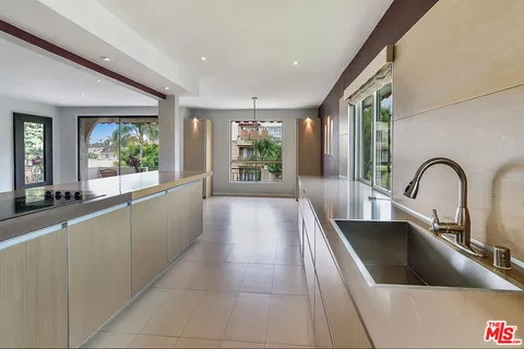 a large kitchen with kitchen island a large window cabinets a sink and stainless steel appliances