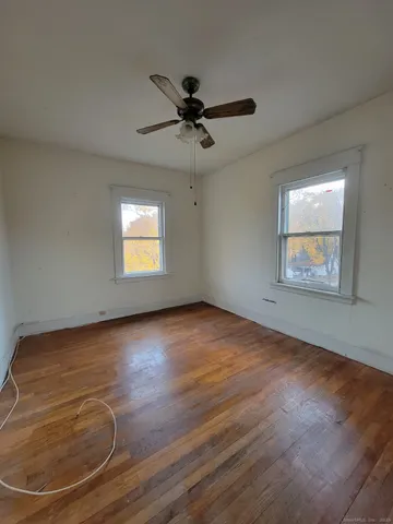 an empty room with wooden floor ceiling fan and windows