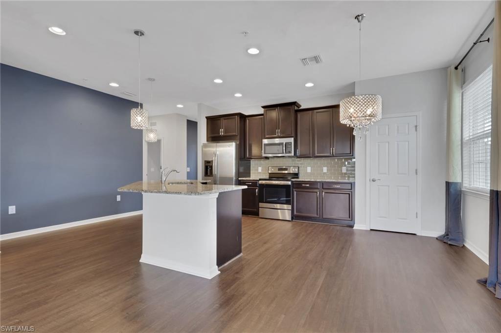 18320 Creekside Preserve Loop, Unit 201 Fort Myers, FL 33908 - Photo 3 of 27 Kitchen featuring a chandelier, appliances with stainless steel finishes, dark brown cabinets, hanging light fixtures, and light stone counters