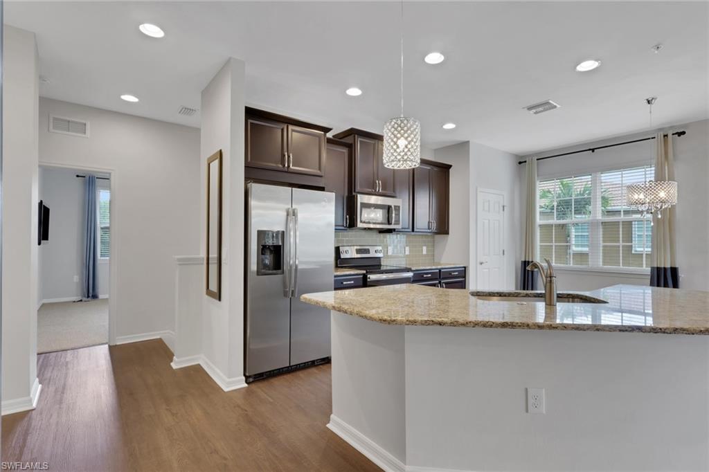 18320 Creekside Preserve Loop, Unit 201 Fort Myers, FL 33908 - Photo 4 of 27 Kitchen with dark brown cabinetry, stainless steel appliances, backsplash, light stone countertops, and hanging light fixtures