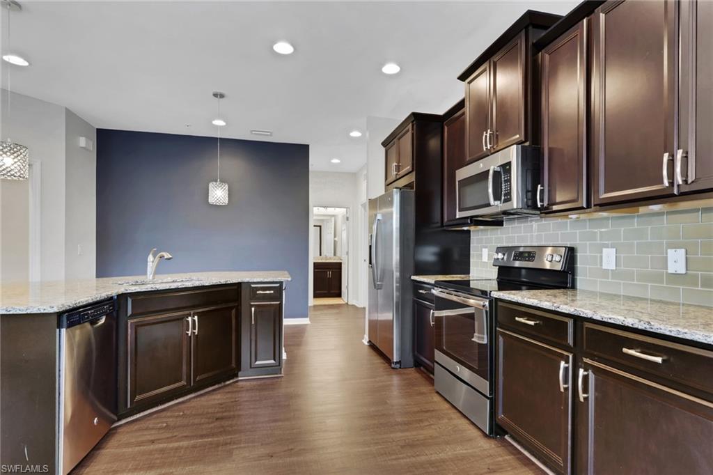 18320 Creekside Preserve Loop, Unit 201 Fort Myers, FL 33908 - Photo 6 of 27 Kitchen with dark brown cabinetry, stainless steel appliances, light stone countertops, recessed lighting, and decorative light fixtures