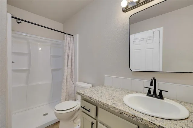 a bathroom with a granite countertop sink toilet a mirror and shower