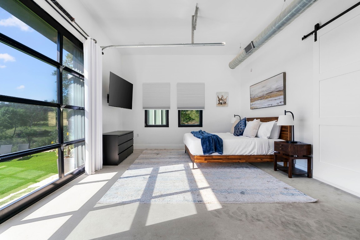 12701 Trails End Road Leander, TX 78641 - Photo 14 of 18 Primary bedroom featuring a king-size bed, concrete floors, large window and overhead door for natural light, wall-mounted TV and closet area.