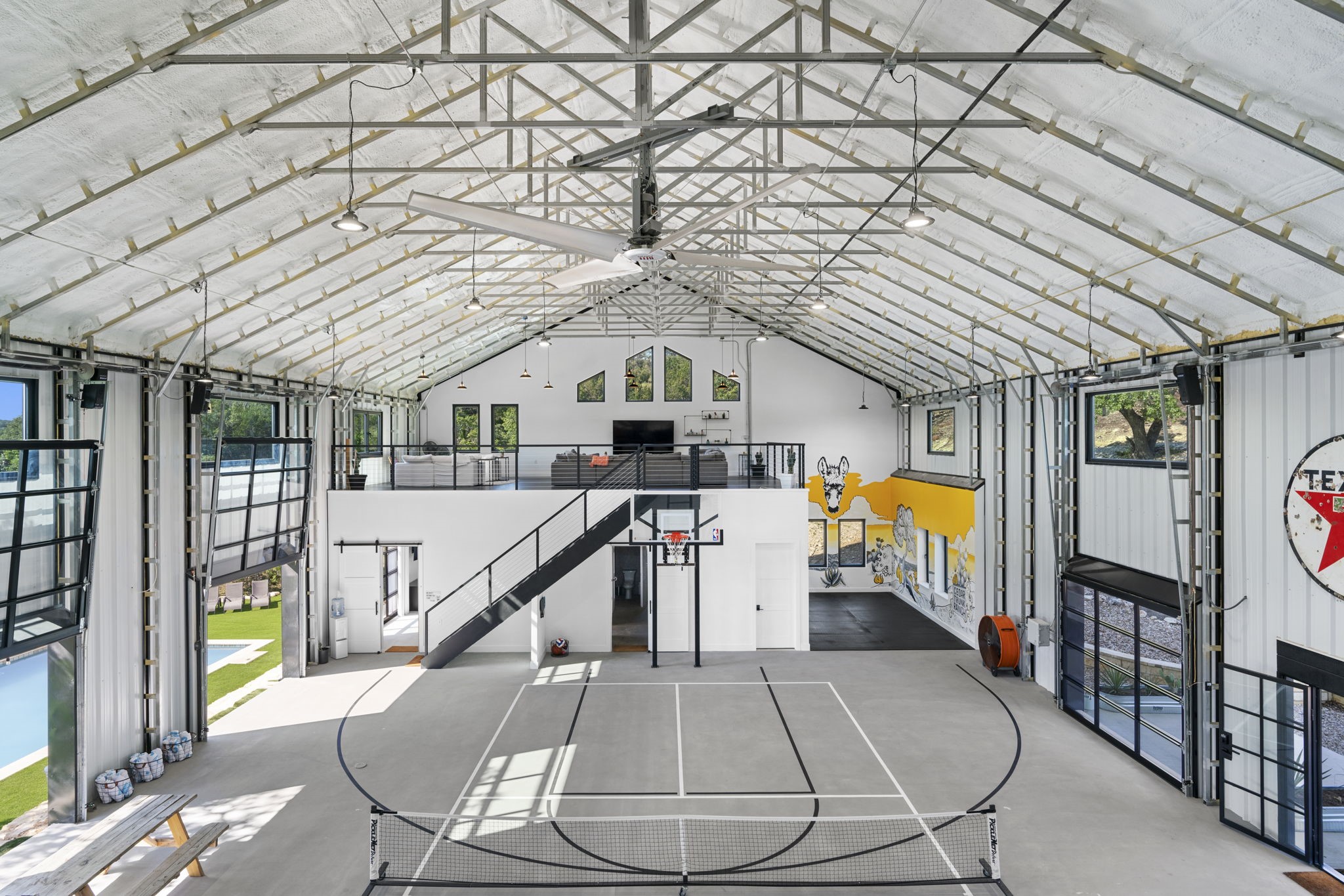 12701 Trails End Road Cedar Park, TX 78613 - Photo 7 of 18 Interior of the indoor recreation building featuring a full-size basketball court, open mezzanine level and large overhead doors for indoor-outdoor use.