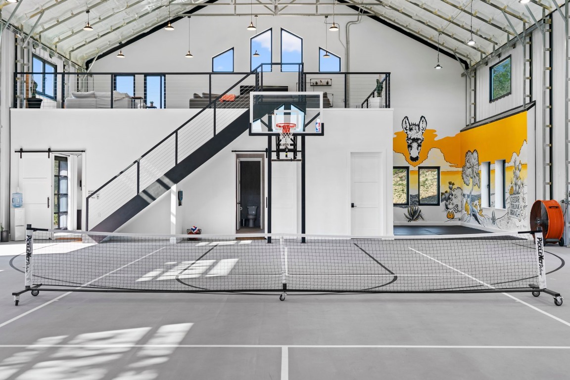 12701 Trails End Road Leander, TX 78641 - Photo 9 of 18 Interior of the indoor recreation building featuring a full-size basketball court, open mezzanine level and large overhead doors for indoor-outdoor use.