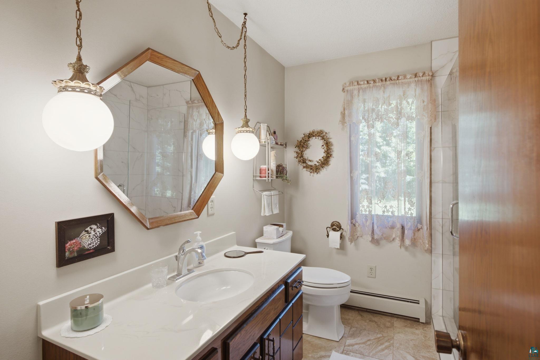 27485 South Kane Road Ashland, WI 54806 - Photo 18 of 35 Bathroom featuring an expansive vanity with a white countertop and integrated sink, an octagonal framed mirror, two pendant light fixtures, and a shower enclosure with glass and tiled walls