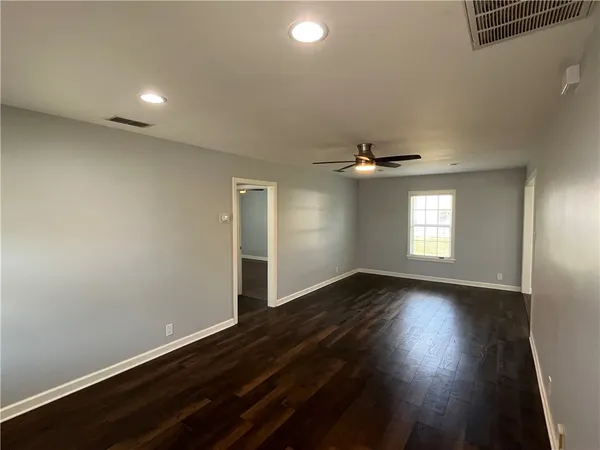 an empty room with wooden floor chandelier fan and windows