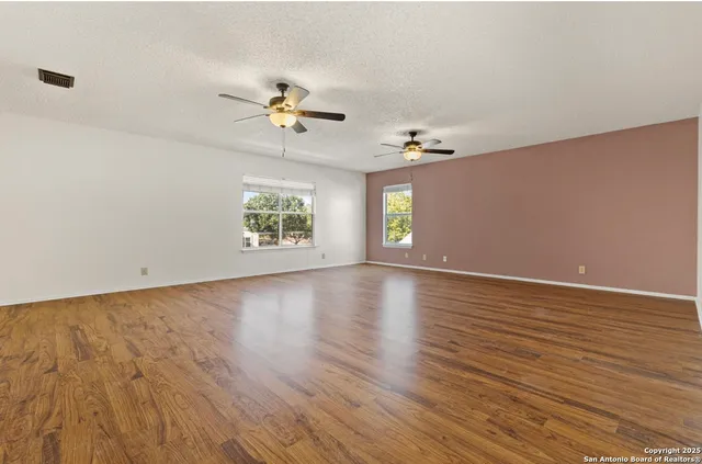 an empty room with wooden floor chandelier fan and windows