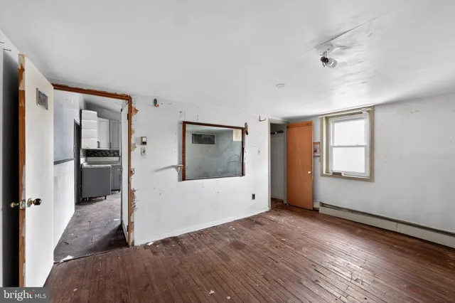 a view of an empty room with wooden floor and a kitchen