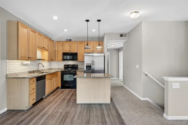 a kitchen with stainless steel appliances granite countertop a refrigerator a stove top oven a sink dishwasher and a refrigerator with wooden floor