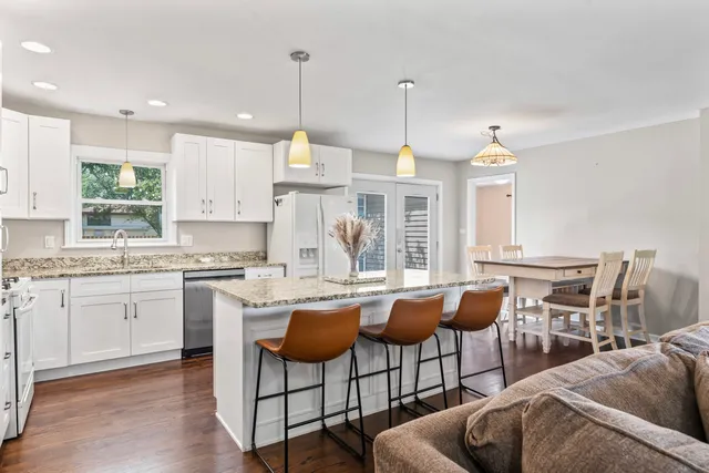 a open kitchen with stainless steel appliances granite countertop a stove a sink a dining table and chairs with wooden floor