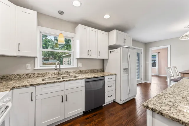 a kitchen with stainless steel appliances granite countertop a refrigerator a sink dishwasher a stove and white countertops with wooden floor