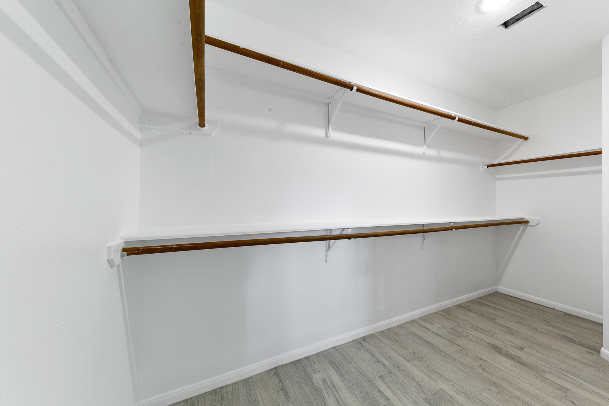 12014 Raven View Drive Houston, TX 77067 - Photo 23 of 29 This photo shows a spacious walk-in closet with wooden shelves and hanging rods, featuring light-colored laminate flooring and white walls, offering ample storage space.