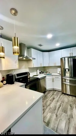 a kitchen with stainless steel appliances a stove a sink dishwasher a refrigerator and white cabinets with wooden floor