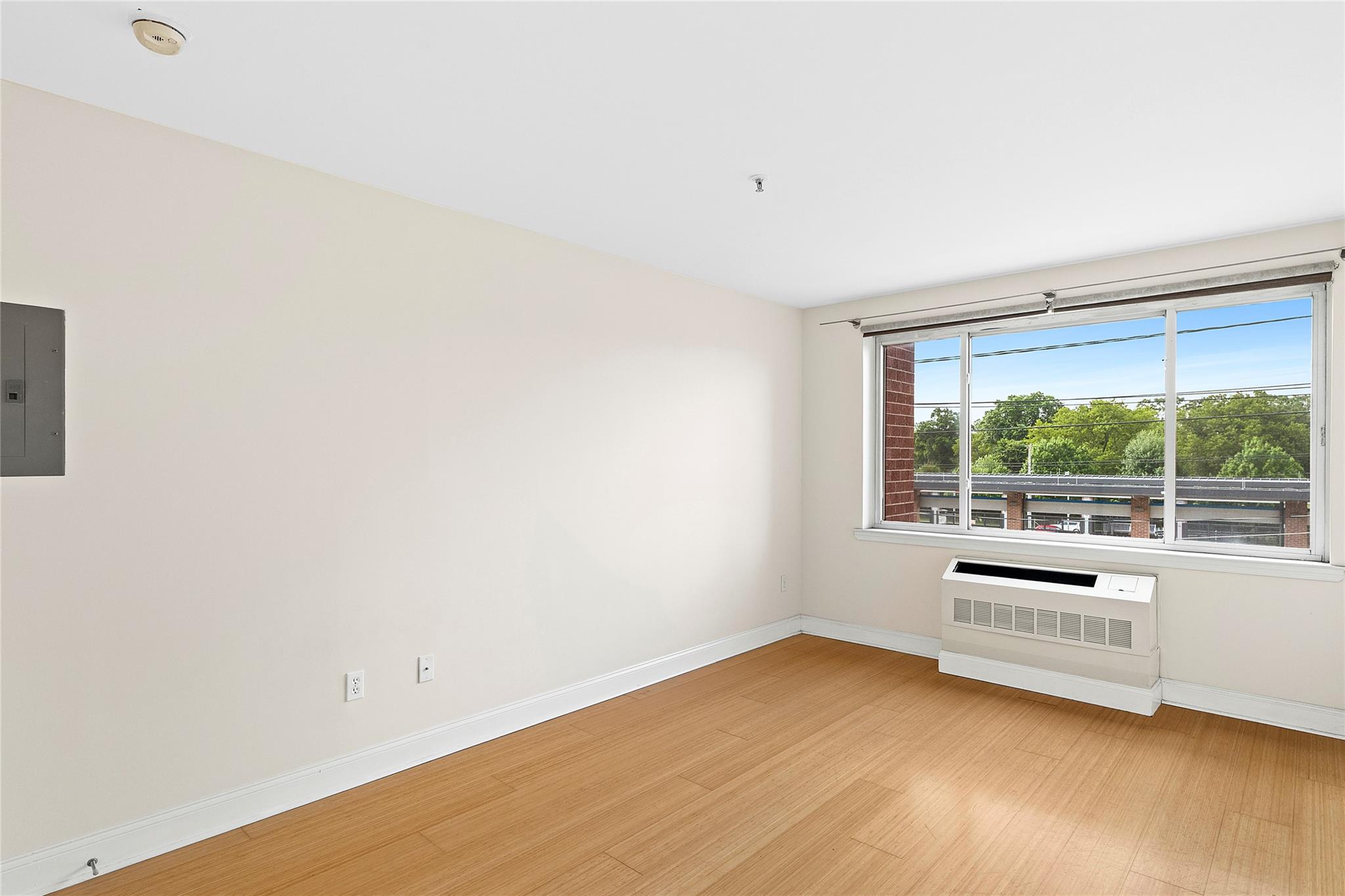130 Post Avenue, Unit 316 Westbury, NY 11590 - Photo 7 of 15 Unfurnished room featuring radiator heating unit, light wood-type flooring, and electric panel
