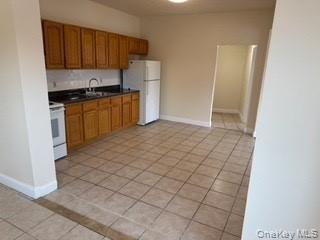 390 Main Street, Unit 3 Beacon, NY 12508 - Photo 2 of 8 Kitchen with dark countertops, brown cabinetry, a sink, white appliances, and baseboards