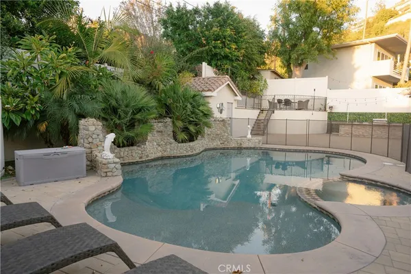 a view of a fountain in the front of a yard with plants and large trees