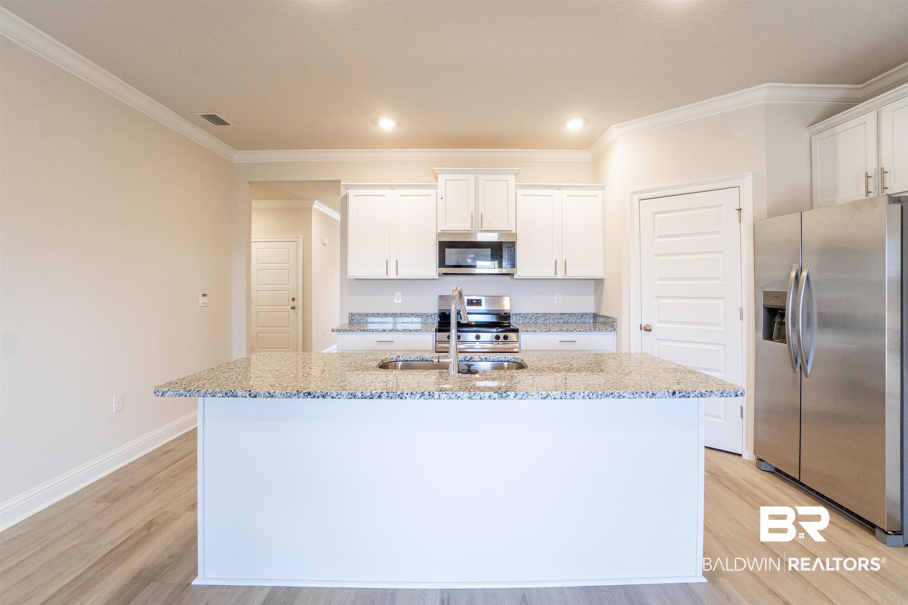1073 Hayward Loop Foley, AL 36535 - Photo 5 of 18 Kitchen island featuring a stainless steel sink with pull-down faucet, granite countertop, white cabinetry, stainless steel appliances, and wood-finish flooring